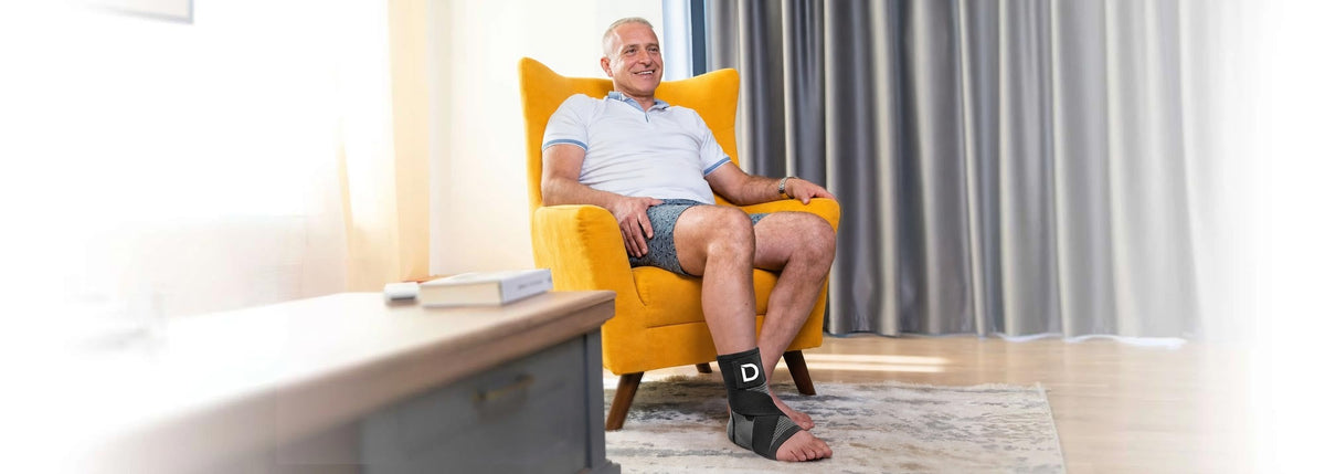 A man relaxing in a yellow armchair with the Dawnlit sleeve on his foot.