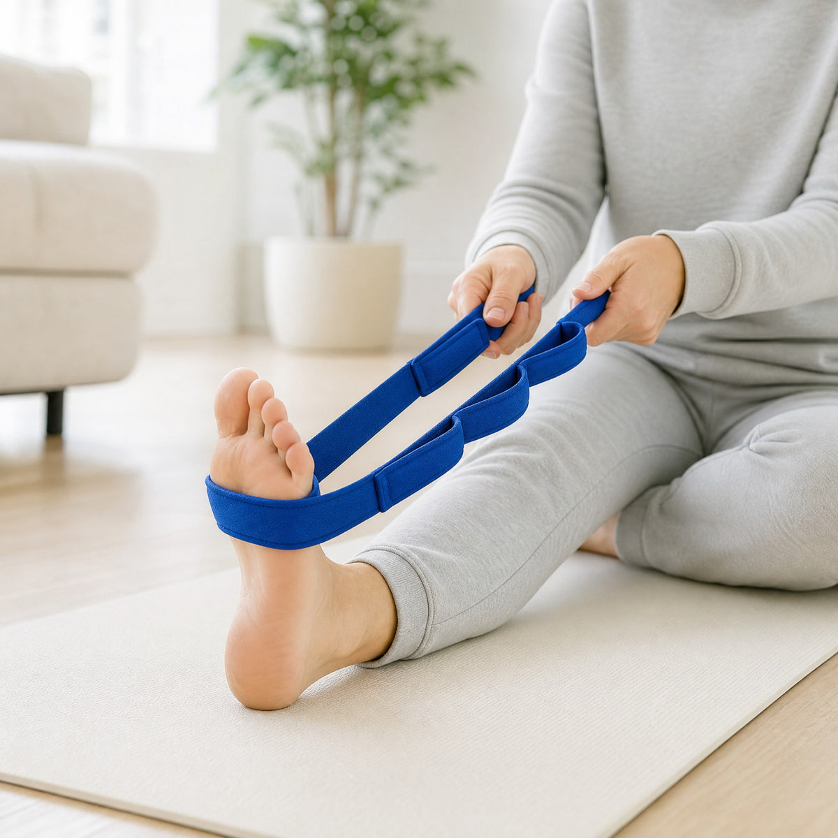 A person sitting on a yoga mat, stretching the foot and calf with the blue padded Dawnlit strap.